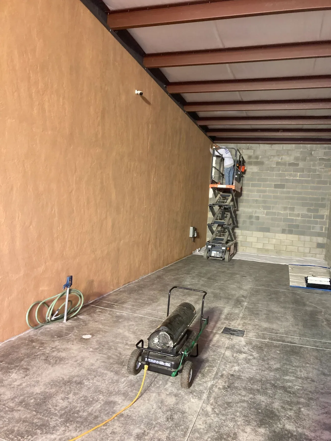 A long tan block wall under a carport roof before painting