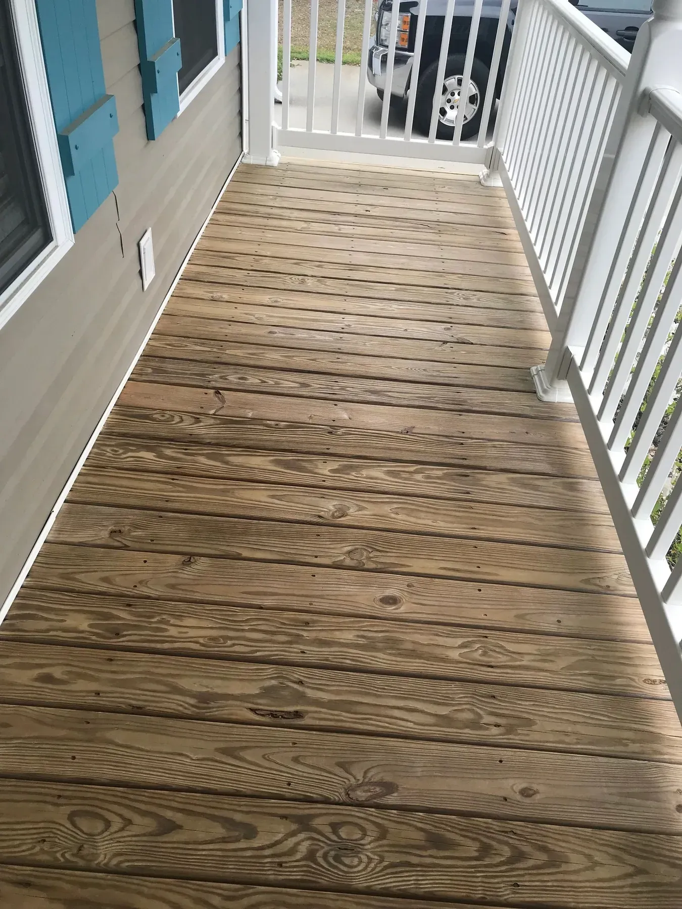 A long front porch with freshly stained pine boards and white rails